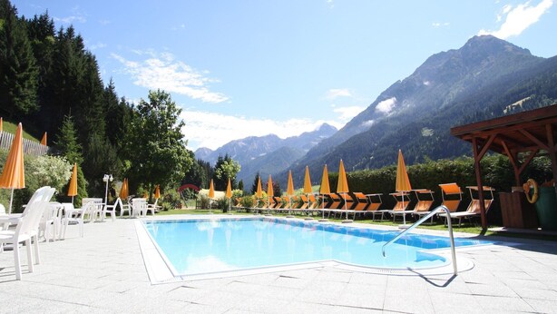 A pool with lounge chairs and umbrellas, surrounded by mountains. - Apartment in Kleinarl near Ski Lift (Kleinarl)