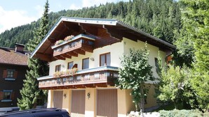 Un chalet traditionnel doté d’un balcon en bois, de nombreuses fenêtres et surplombant un paysage montagneux.