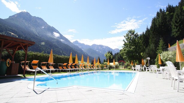 Un espace piscine doté de chaises longues et de parasols, entouré de montagnes.