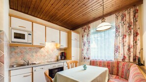 Une cuisine compacte équipée d’un four à micro-ondes, d’une cuisinière et d’un évier. On y trouve une table à manger avec une chaise, ainsi qu’un canapé agrémenté d’un coussin à motifs.
