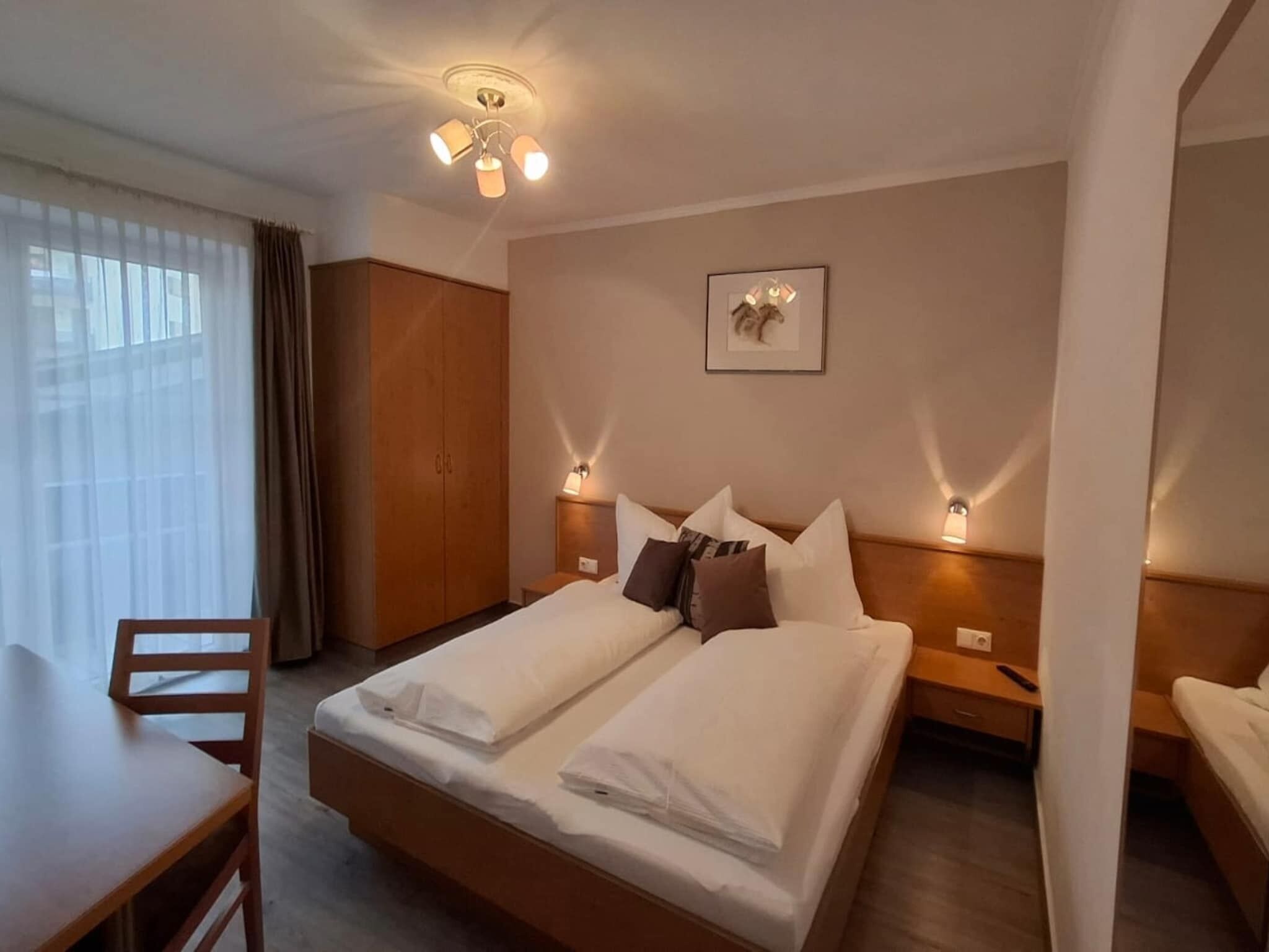 Een hotelkamer met een tweepersoonsbed, een houten bureau, een stoel, een kledingkast en een plafondlamp.