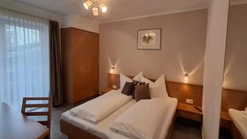 Een hotelkamer met een tweepersoonsbed, een houten bureau, een stoel, een kledingkast en een plafondlamp.