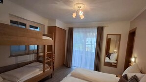 Una habitación de hotel con literas, un ventanal con cortinas, un ventilador de techo y un espejo en la pared.