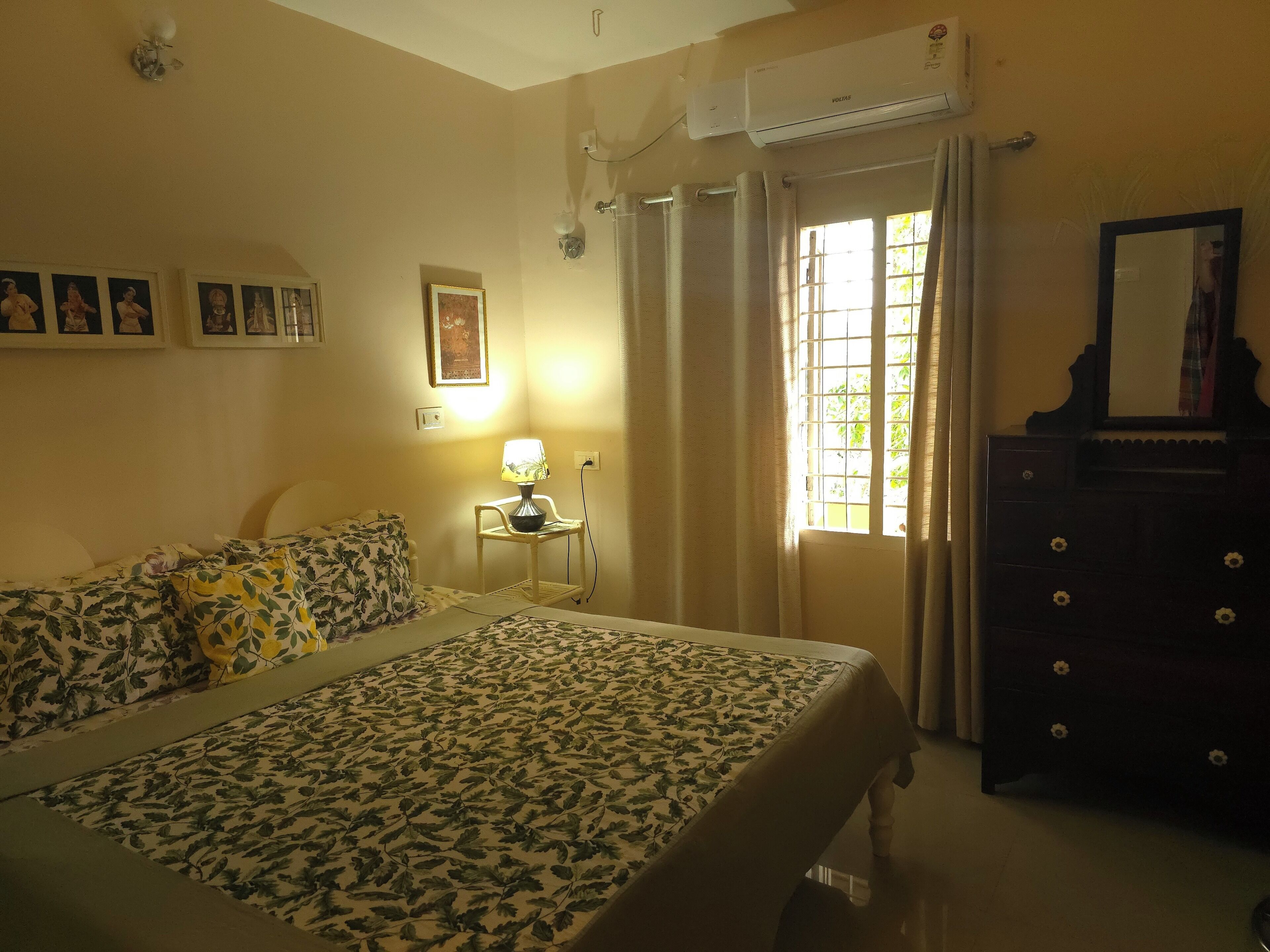Un dormitorio con cama, mesita de noche, cómoda, ventana con cortinas y aire acondicionado instalado en la pared.