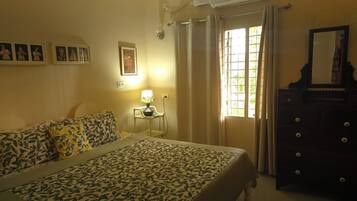 Un dormitorio con cama, mesita de noche, cómoda, ventana con cortinas y aire acondicionado instalado en la pared.