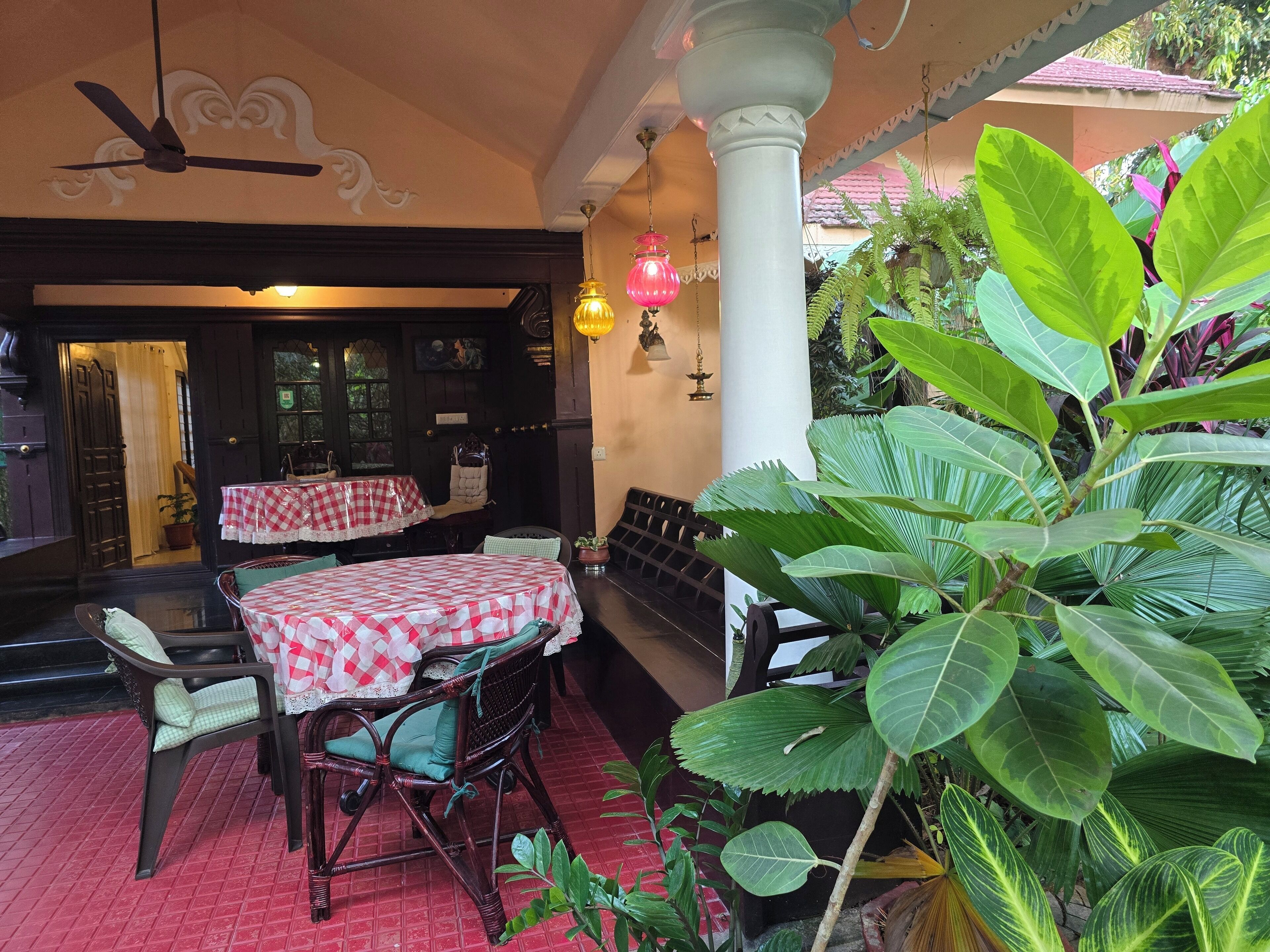 An outdoor seating area with checkered tablecloths and wicker chairs, surrounded by lush green plants.