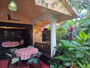 An outdoor seating area with tables covered in checkered tablecloths, wicker chairs, and a ceiling fan. - Bella Boutique Homestay (Alappuzha)