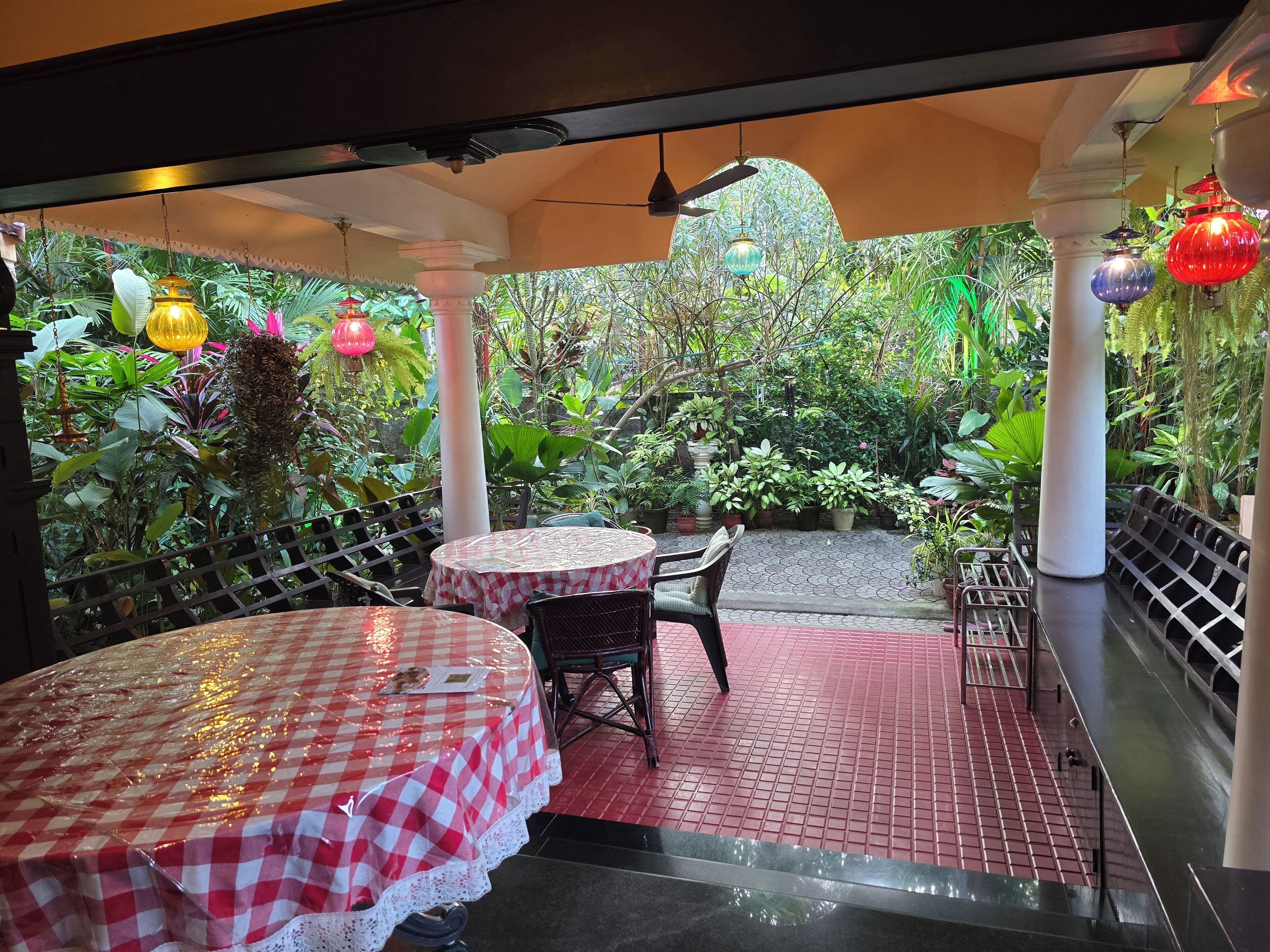 An indoor garden with tables and chairs, surrounded by lush greenery and decorative hanging lights.