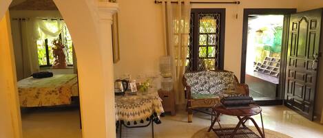 A room with a bed, a sofa, a table with a vase, and a door leading outside.