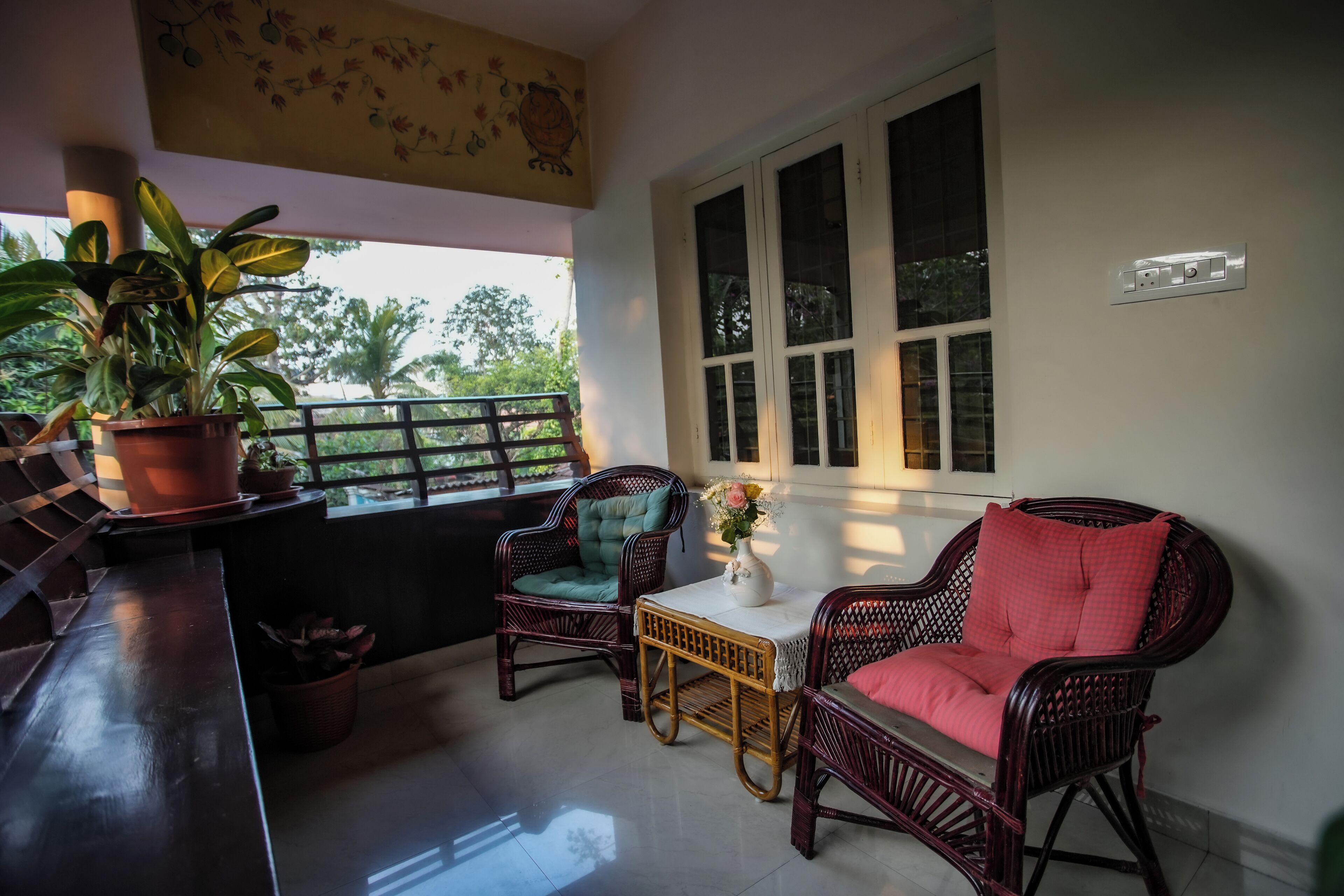 A balcony with wicker furniture, a potted plant, and a view of trees.