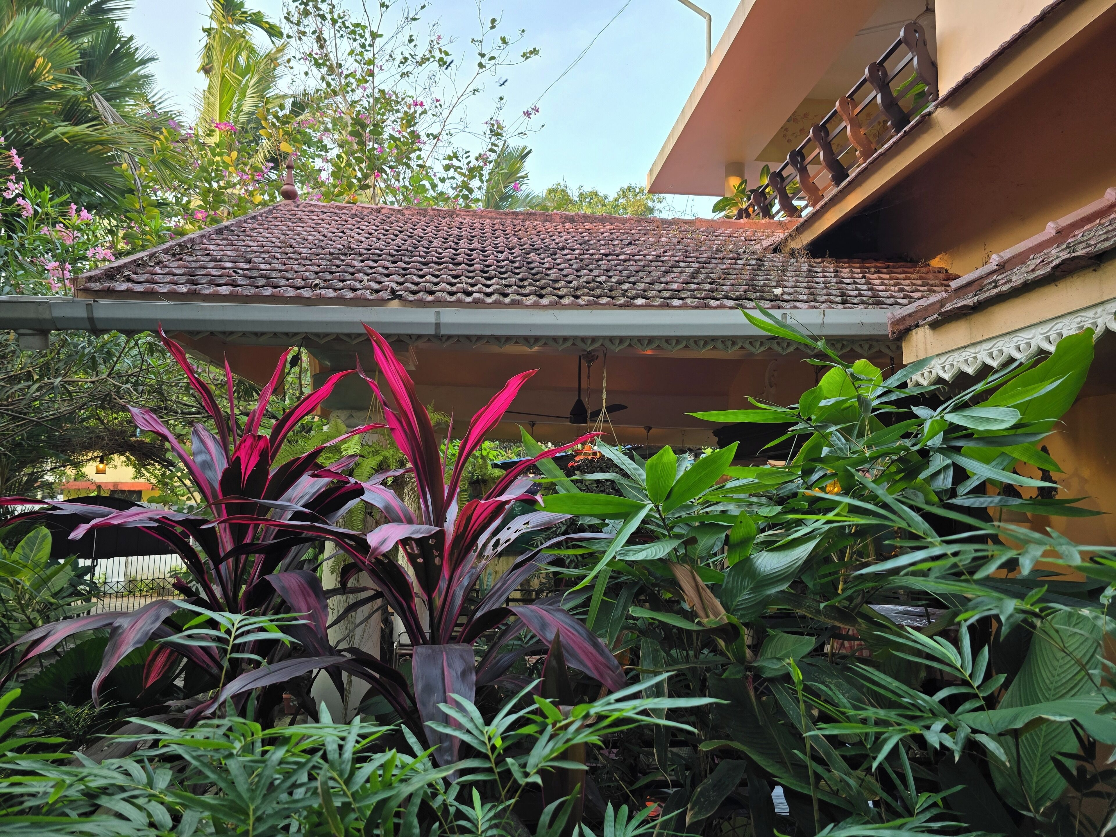 A traditional building with a tiled roof, surrounded by lush greenery and flowering plants.