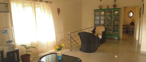 A living room with a glass-top table, wicker chairs, a bookshelf, and a water dispenser.