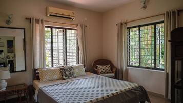 A bedroom with a bed, a chair, a desk, and two windows with curtains.