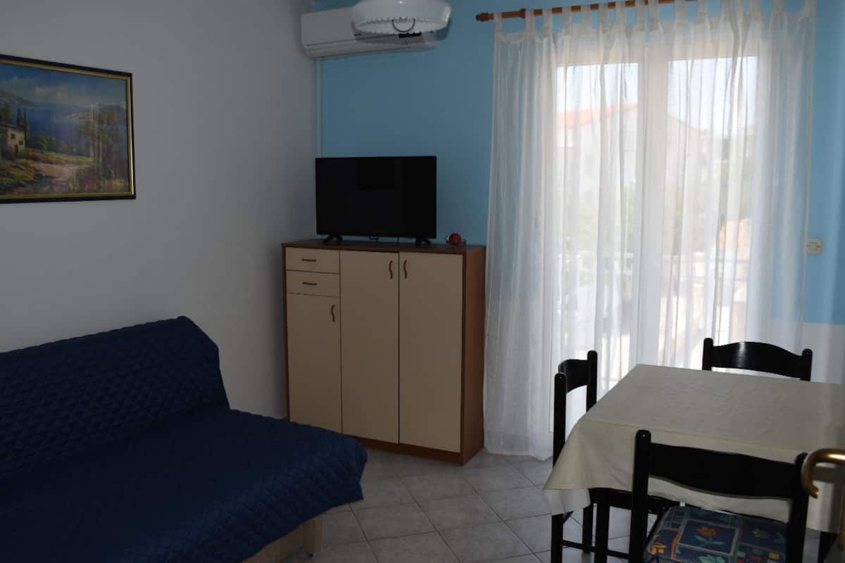 A room with a bed, a table with chairs, a television on a cabinet, and a window with curtains.