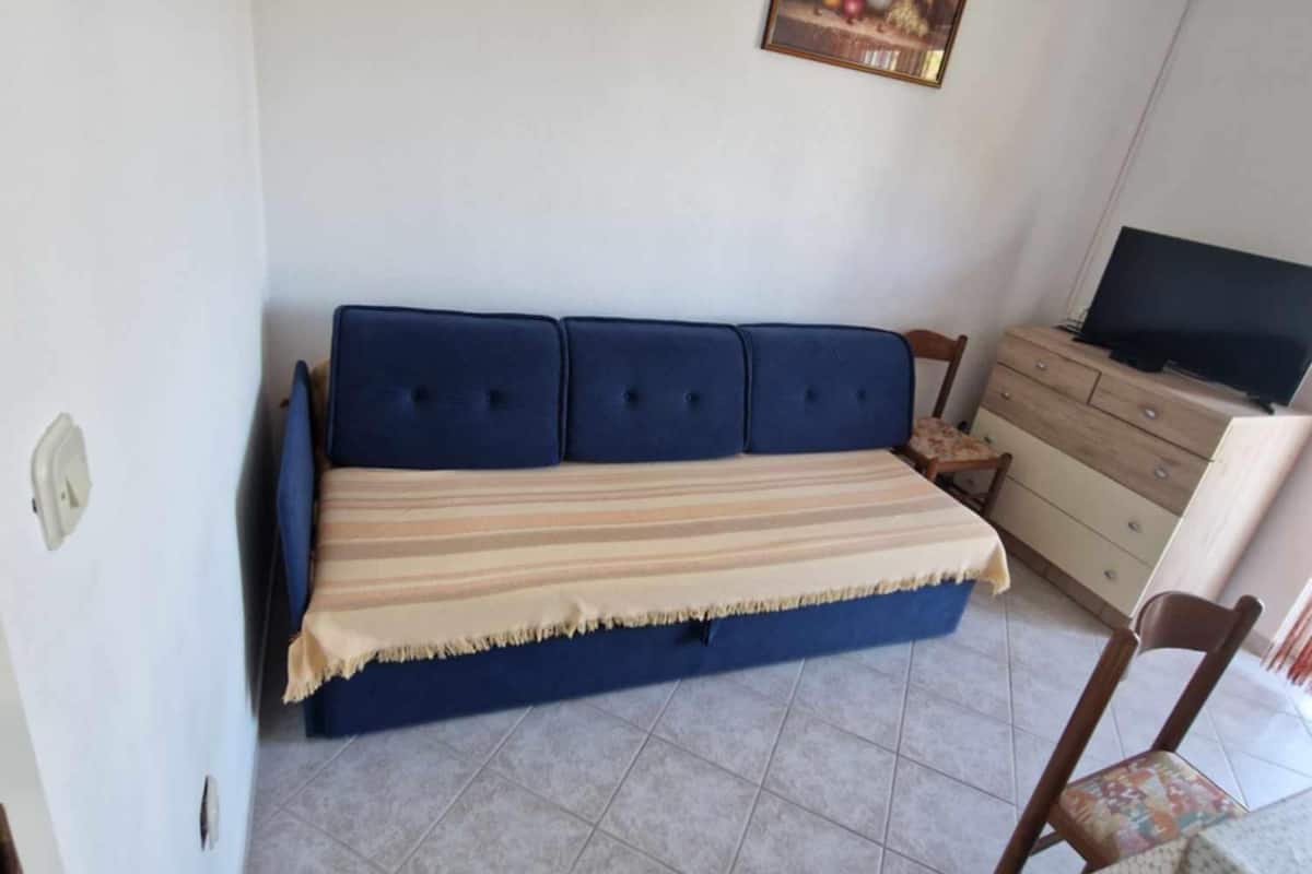 A bedroom with a blue sofa bed, a wooden dresser, and a television.