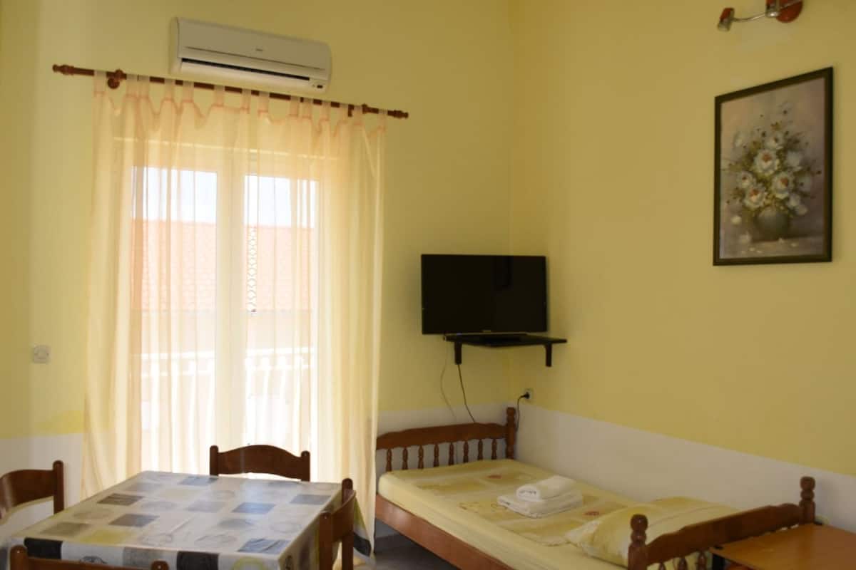 A room with a bed, a table, chairs, an air conditioner, a television, and a painting on the wall.
