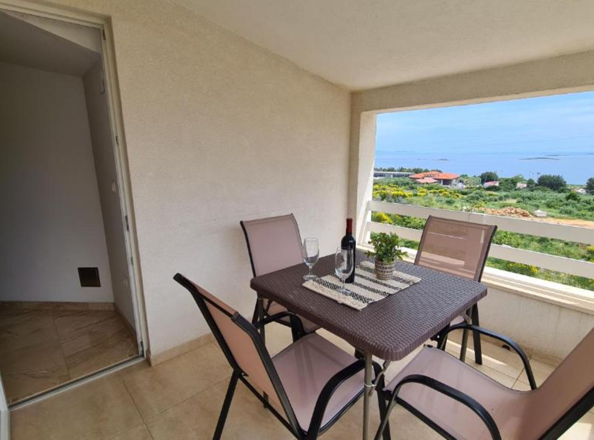 Un balcón con una mesa y sillas, una botella de vino y vistas al mar y vegetación.