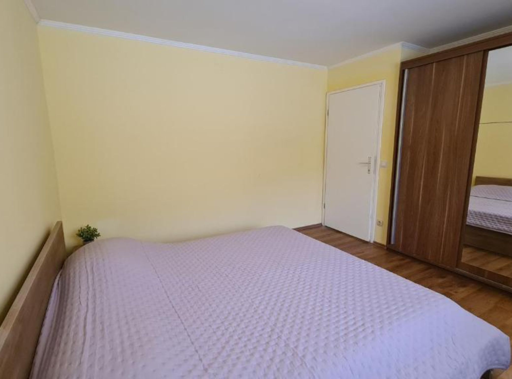 A bedroom with a bed, a wooden wardrobe, and a door.