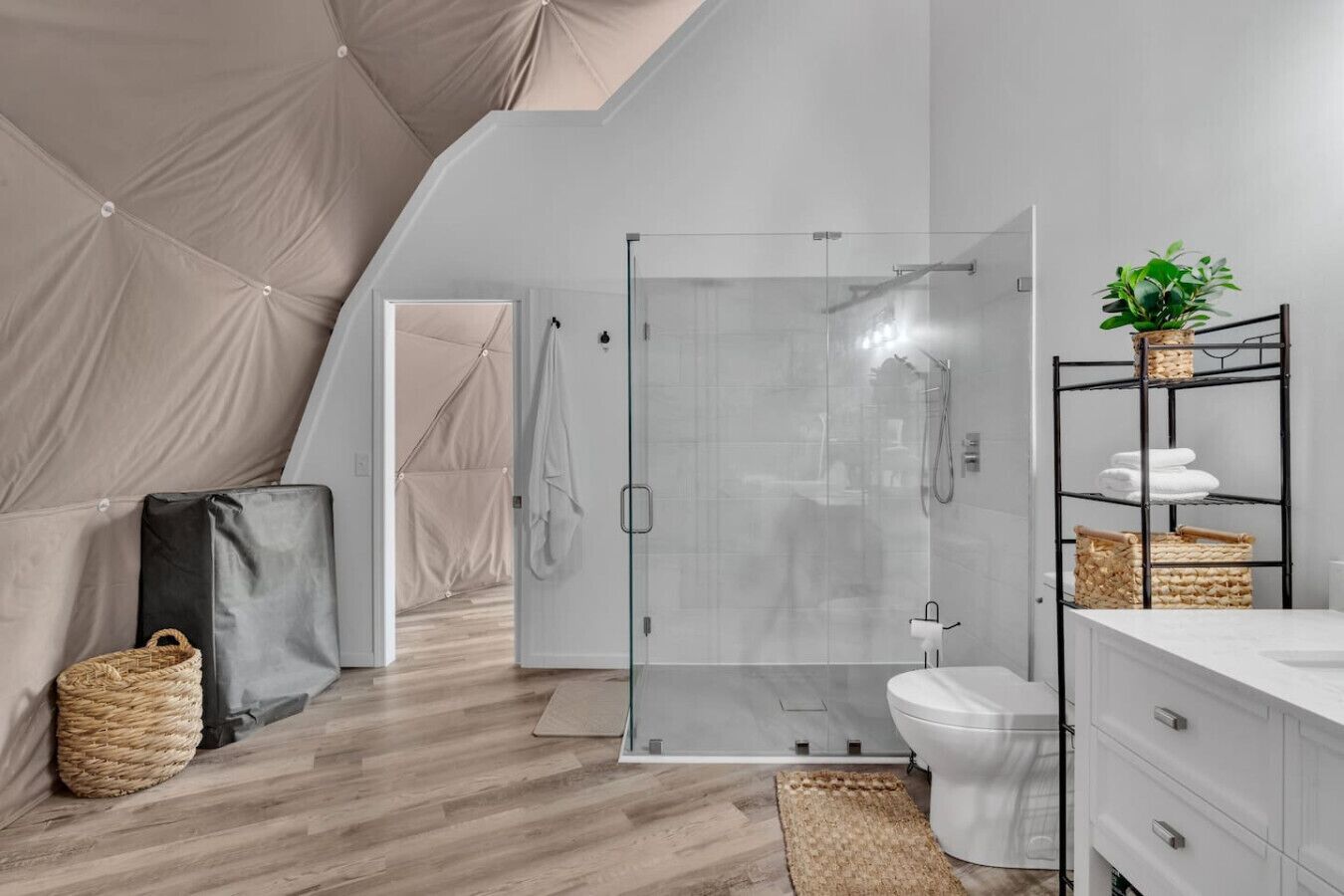 A modern bathroom with a glass shower enclosure, a white toilet, and a vanity with storage baskets.