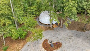A geodesic dome structure surrounded by dense forest, with a small garden area in the foreground. - Nottely River Retreat | Fire Pit (Murphy)