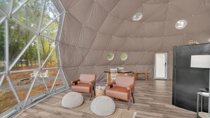 A spacious tent with a high ceiling, two leather chairs, a small table, and a refrigerator. - Nottely River Retreat | Fire Pit (Murphy)