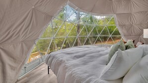 A tented room with a bed, a view of trees through a geometric window, and a wooden floor. - Nottely River Retreat | Fire Pit (Murphy)