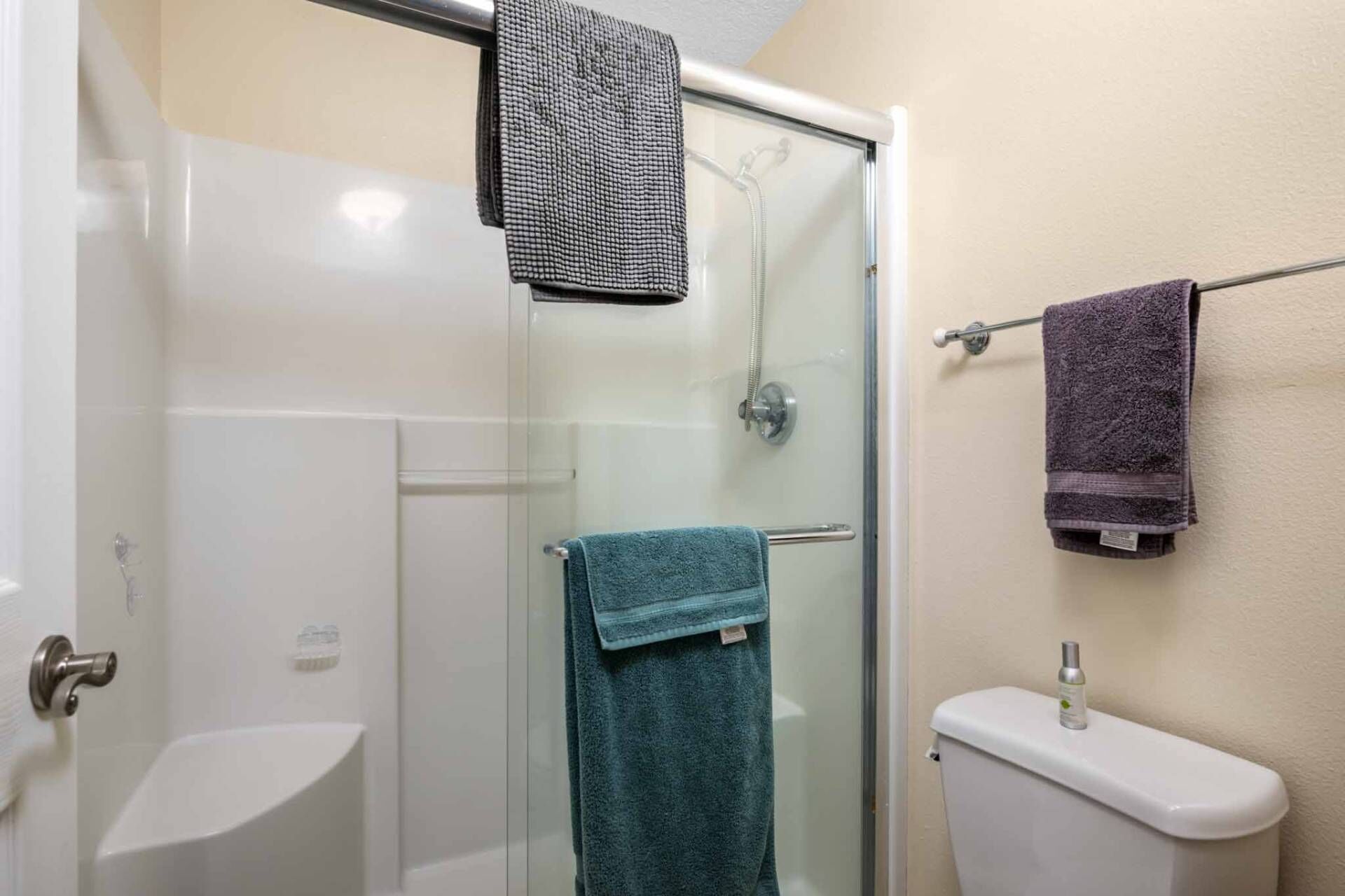 Een badkamer met een douchecabine van glas, een wit toilet en twee handdoeken aan de muur.