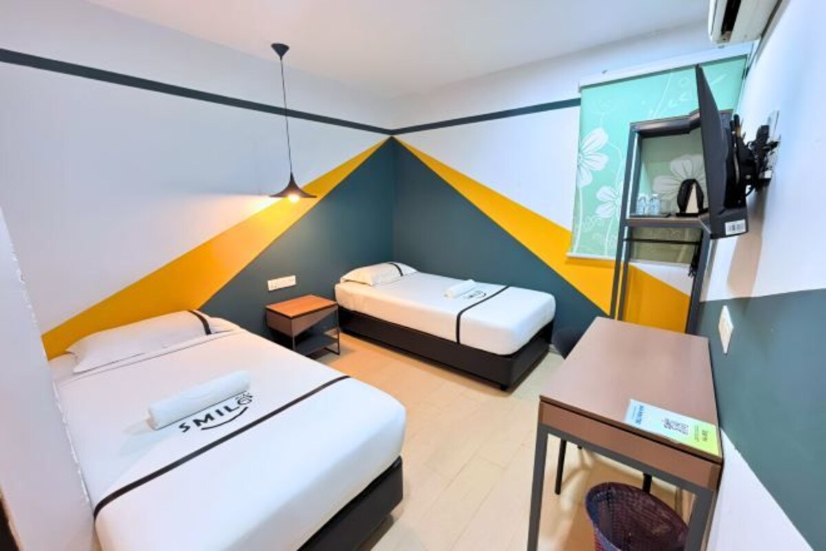 Une chambre d’hôtel avec deux lits, un bureau, une chaise, une télévision et une petite étagère avec quelques objets.