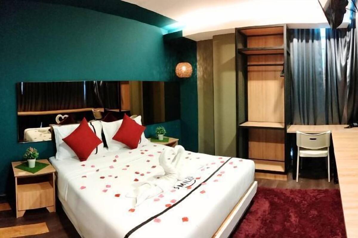 Une chambre d’hôtel avec un lit, un bureau, une chaise, un miroir et un tapis rouge.