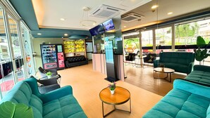 Una hall d'albergo con divani color acquamarina, una televisione, distributori automatici e la reception.