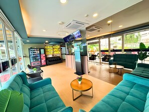 A hotel lobby with teal sofas, a TV, vending machines, and a reception desk.