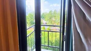 Une porte de balcon ouverte, donnant sur un paysage verdoyant et des bâtiments.