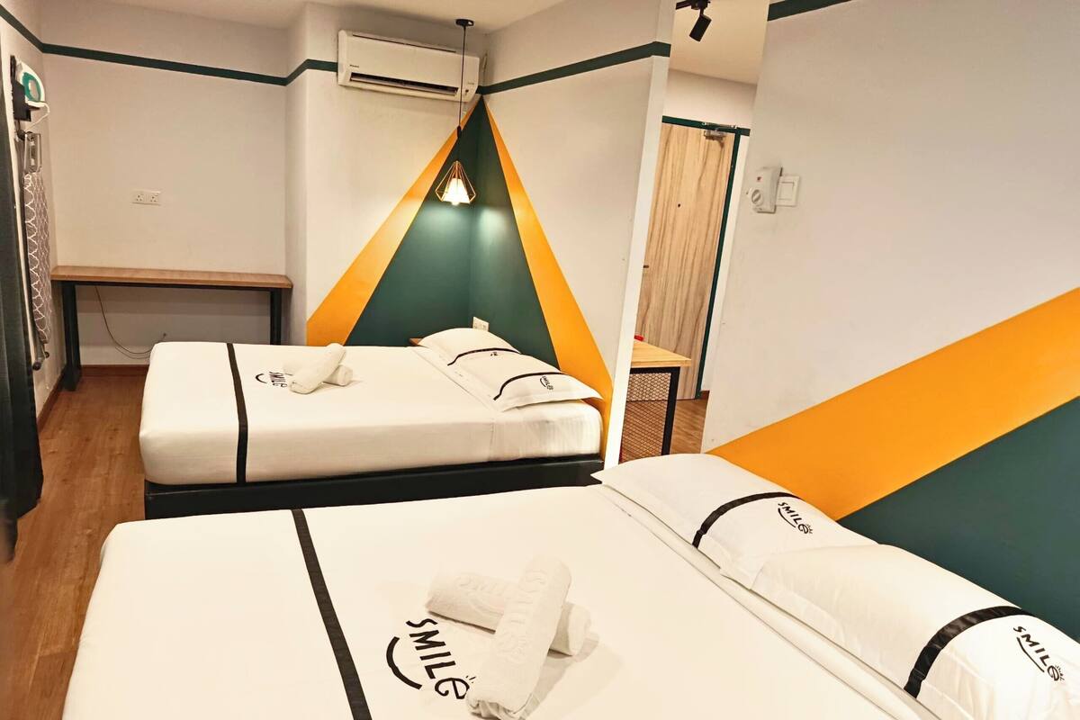 Une chambre d’hôtel avec deux lits, un plancher en bois, un appareil de climatisation et un décor mural aux couleurs verte et orange.