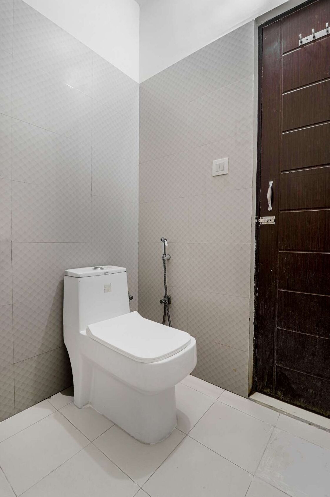 A bathroom with a white toilet, a shower, and a dark wooden door.
