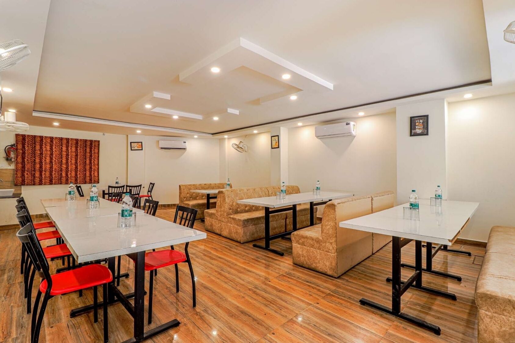A conference room with a long table, several chairs, and a sofa. There are air conditioning units on the walls and a fire extinguisher on the wall.