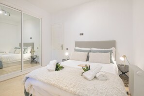 A neatly made bed with a white comforter and pillows, a bedside table with a lamp, and a large mirror on the wall. - Puerto Banus Near La Sala By The Sea (Marbella)