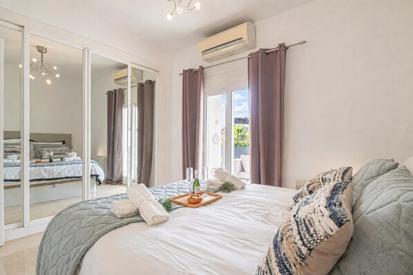 Un espacioso dormitorio con una cama grande, una puerta corrediza de vidrio que da a un balcón y un equipo de aire acondicionado en la pared.
