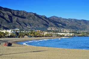 Una playa con montañas al fondo, cielo despejado y una sombrilla.