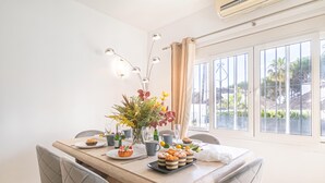 A dining area with a table set for two, featuring a floral centerpiece, a variety of pastries, and a view of the outdoors through large windows. - Puerto Banus Near La Sala By The Sea (Marbella)