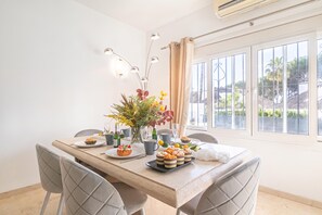 A dining area with a table set for two, featuring a floral centerpiece, a variety of pastries, and a view of the outdoors through large windows. - Puerto Banus Near La Sala By The Sea (Marbella)