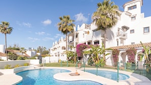 A swimming pool with a curved design, surrounded by a fence, and palm trees in the background. - Puerto Banus Near La Sala By The Sea (Marbella)