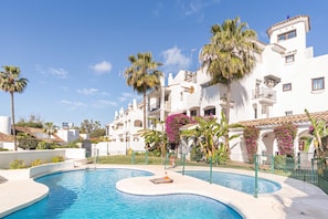 A swimming pool with a curved design, surrounded by a fence, and palm trees in the background. - Puerto Banus Near La Sala By The Sea (Marbella)