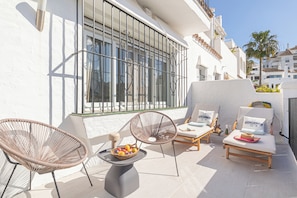 A sunlit outdoor seating area with wicker chairs, a table with fruit, and a lounge chair with a cushion labeled "YACHT CLUB".