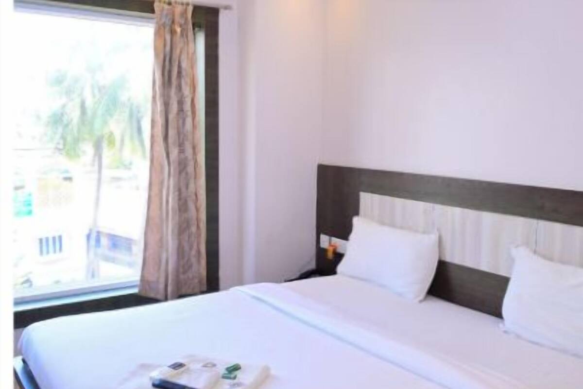 Quarto de hotel com uma cama grande, uma janela com cortinas, um ventilador de teto e um ar condicionado.