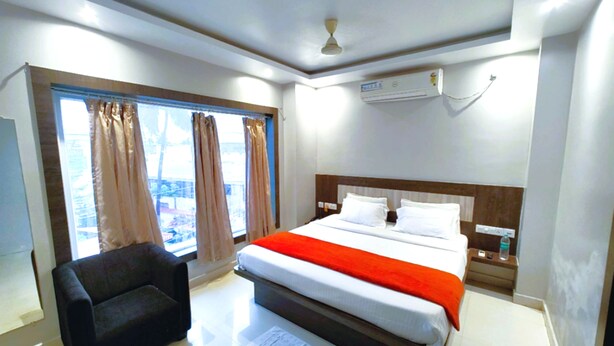 Une chambre d’hôtel équipée d’un lit, d’une chaise, d’une fenêtre avec des rideaux, d’un climatiseur et d’un ventilateur de plafond.