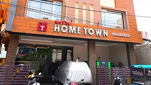 Un hôtel à plusieurs étages, reconnaissable à son grand panneau « HOME TOWN », qui présente une architecture moderne combinant des éléments en brique et des panneaux en bois.