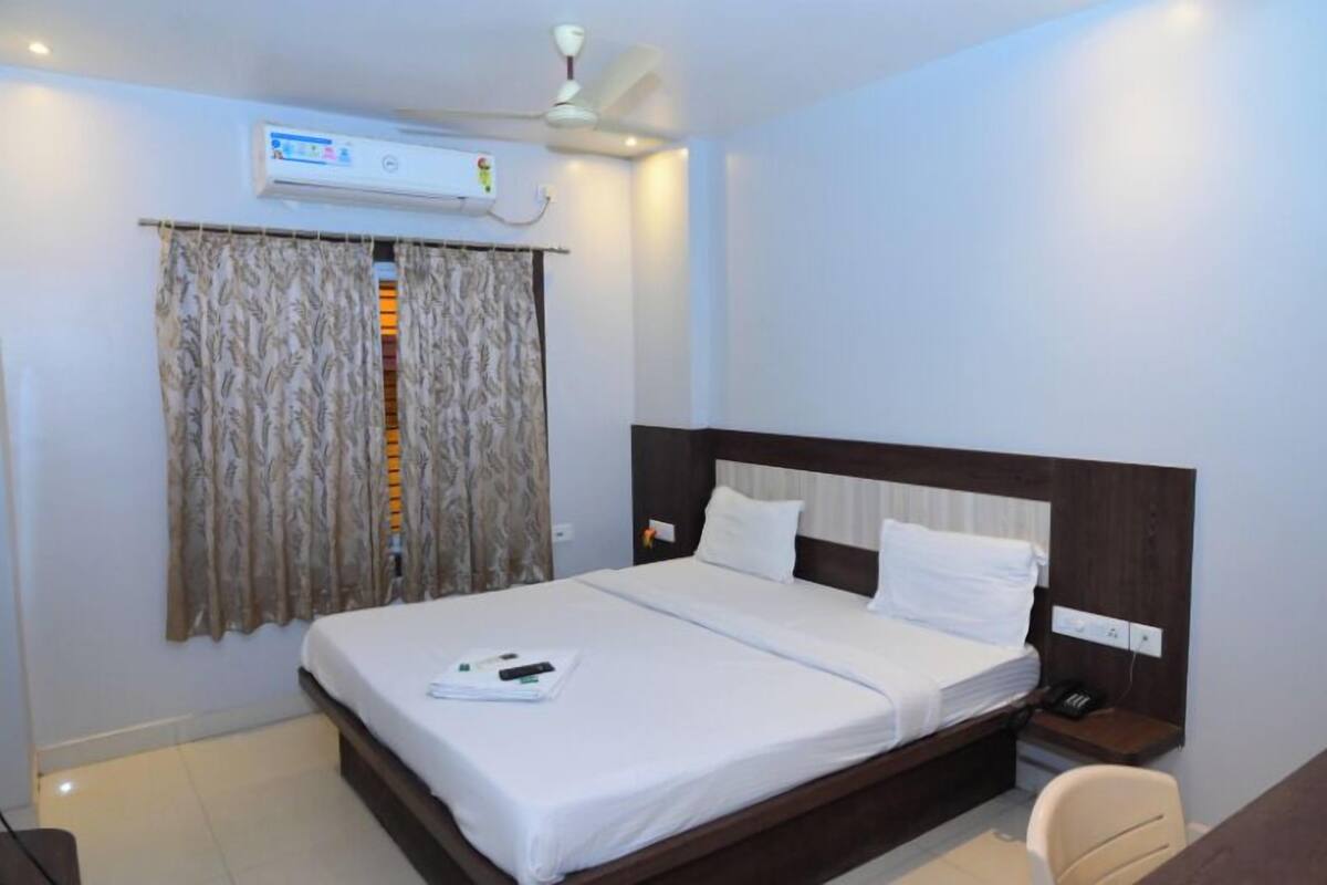 Quarto de hotel com cama, mesa de cabeceira com telefone, ar condicionado e cortinas.