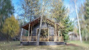 A wooden cabin with a porch, surrounded by trees.