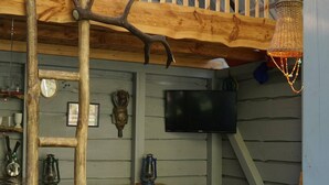 A rustic wooden deck with a high ceiling, a TV mounted on the wall, and a lantern hanging from the ceiling.