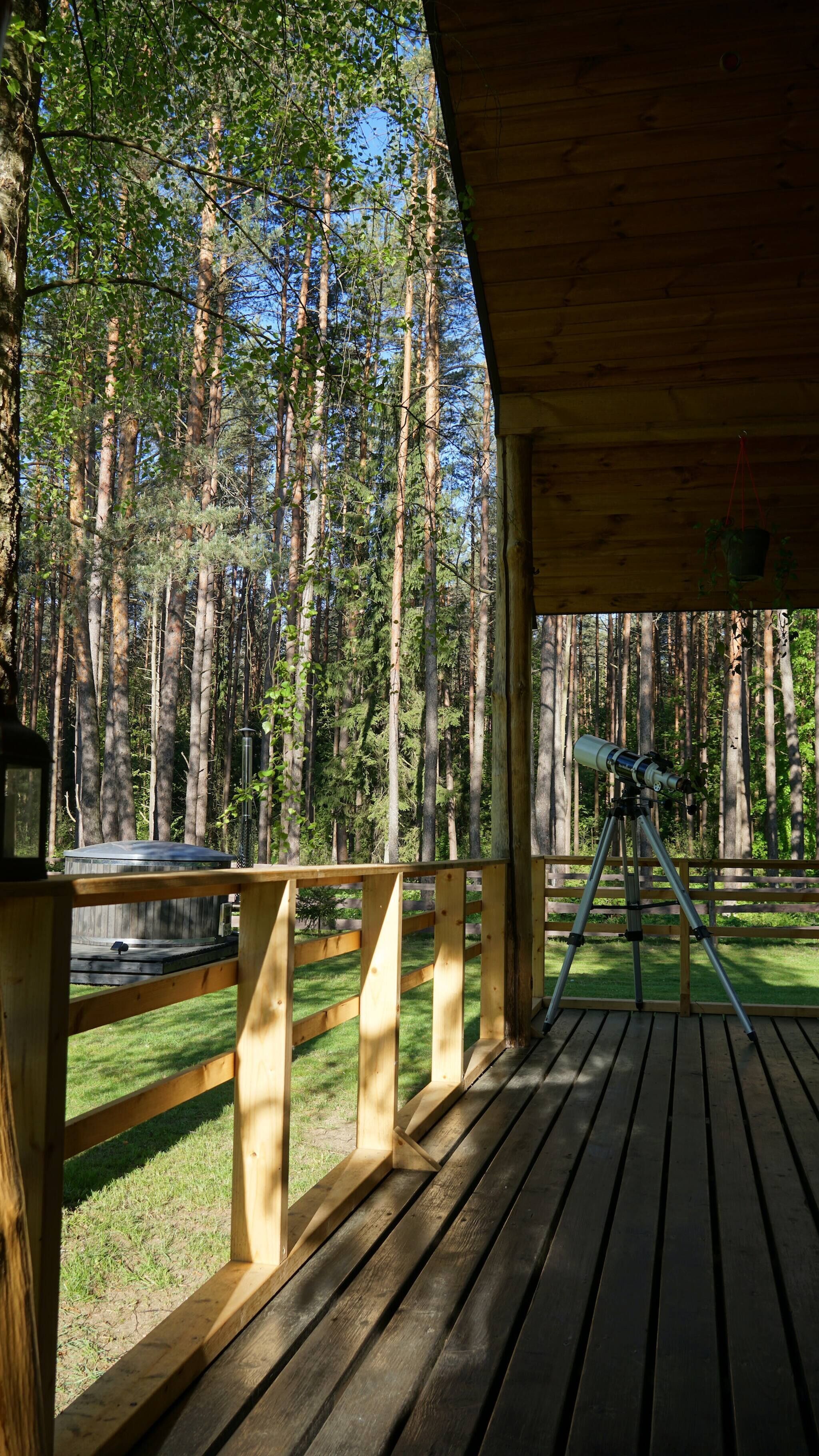 En träveranda med ett teleskop på ett stativ, omgiven av en skog.